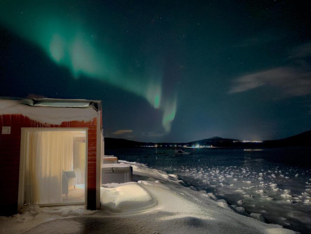 Norwegian Wild in Lapland Noorwegen chalet in de sneeuw met uitzicht over het water.