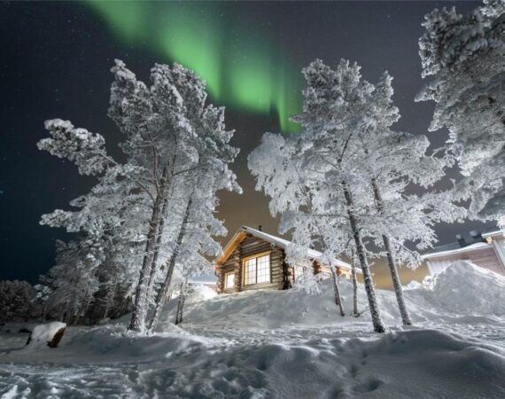 Wilderness Hotel Inari & Igloos in Finland Lapland blokhut in de sneeuw met het noorderlicht op de achtergrond.
